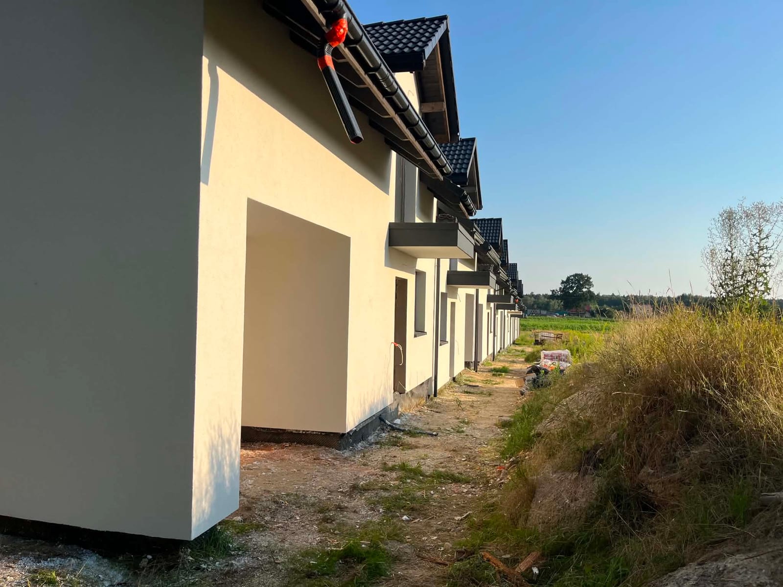 Skończone elewacje zabudowy szeregowej w kremowej bieli, z grafitowymi obróbkami i rynnami